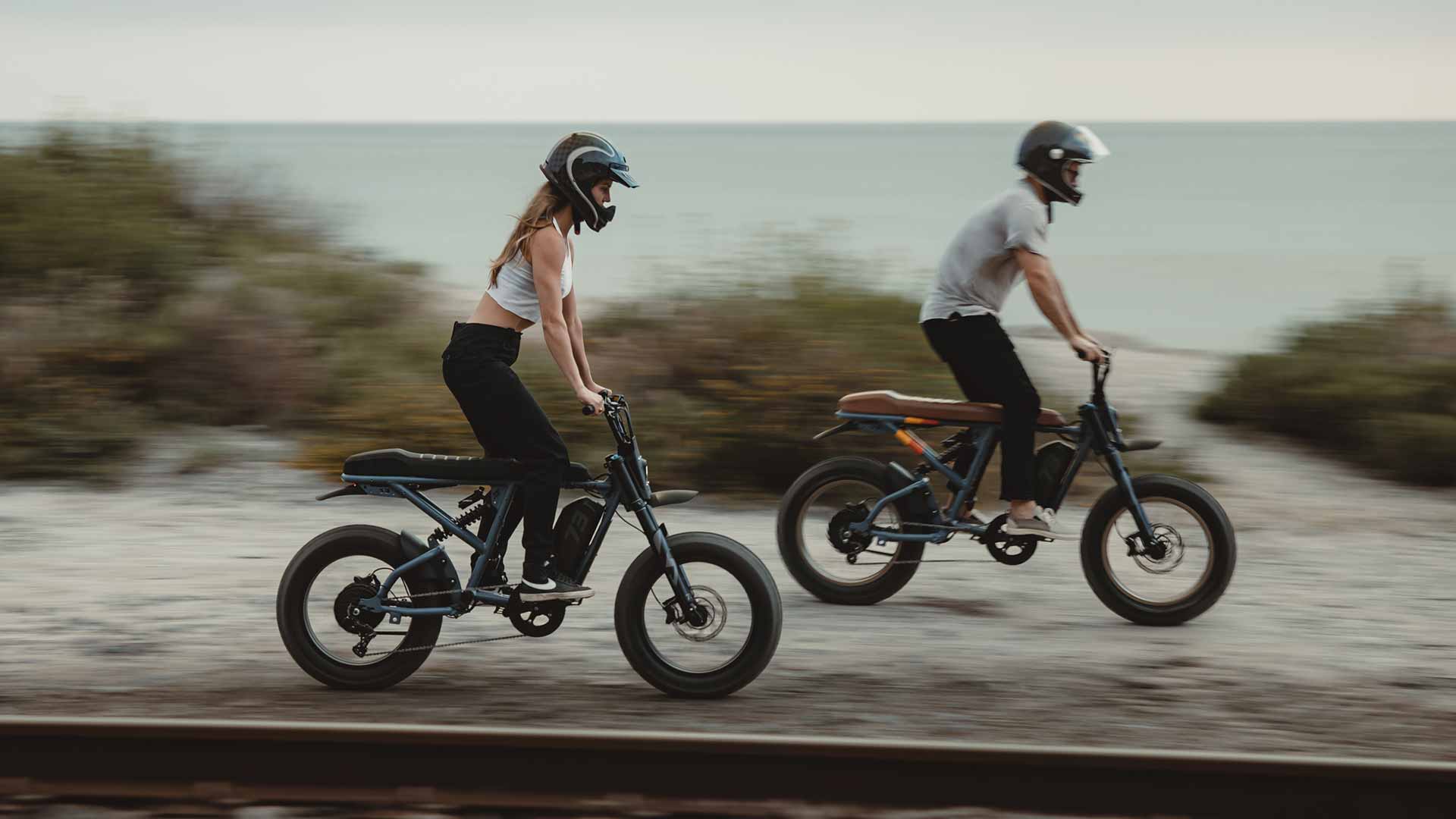 Two young riders on Super73 ebikes cruising along the highway and standing on their pedals