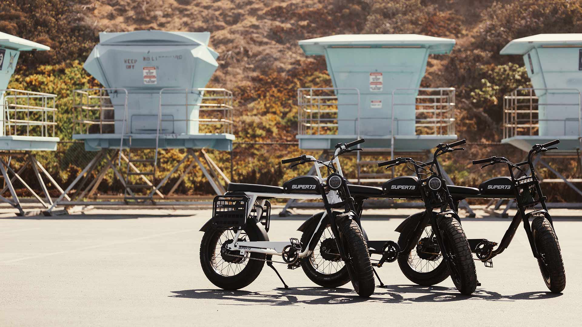 Lineup of Super73 ebikes on the beach in front of lifeguard towers.