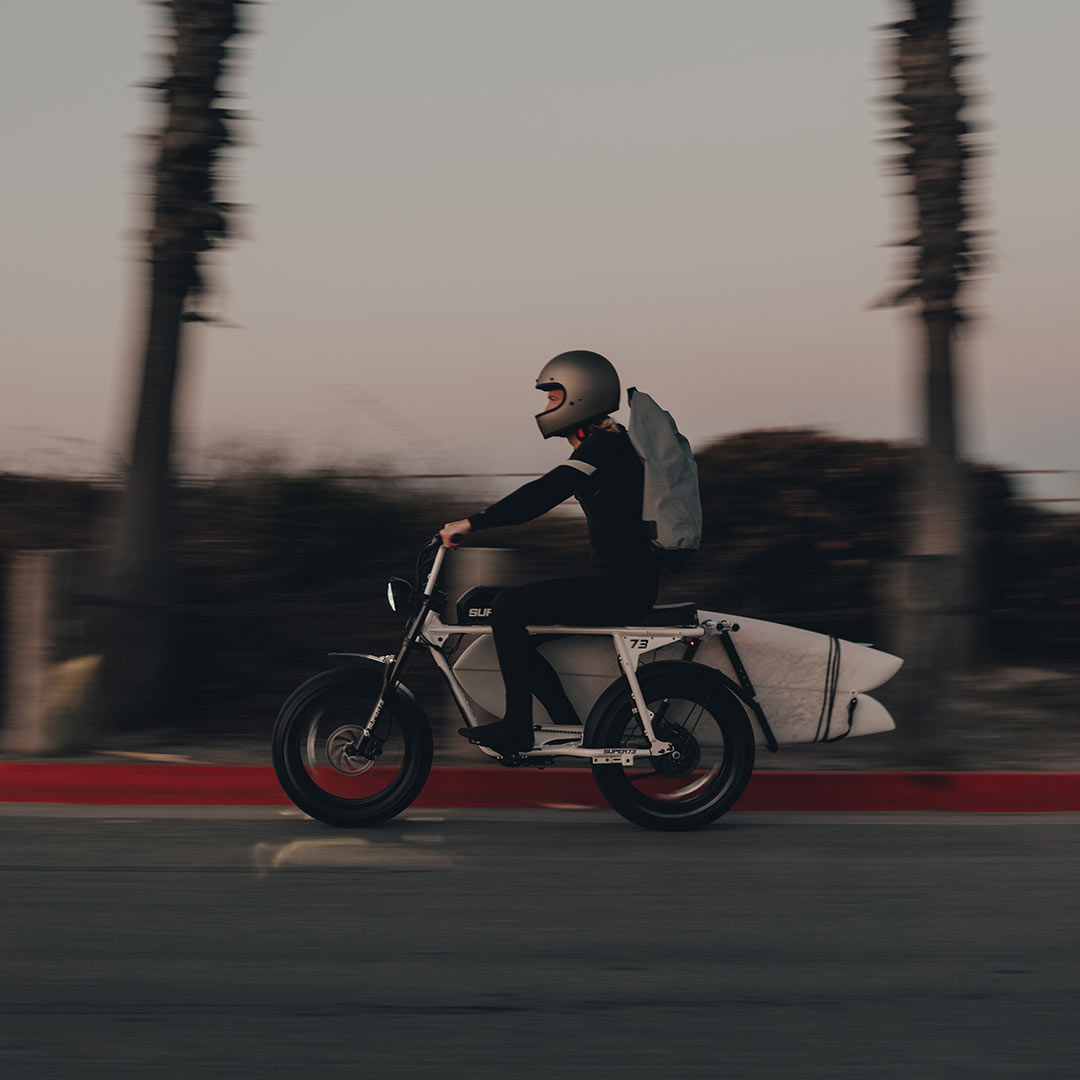 Lifestyle image of SUPER73 rider riding his S2 with a surfboard rack going to the beach.