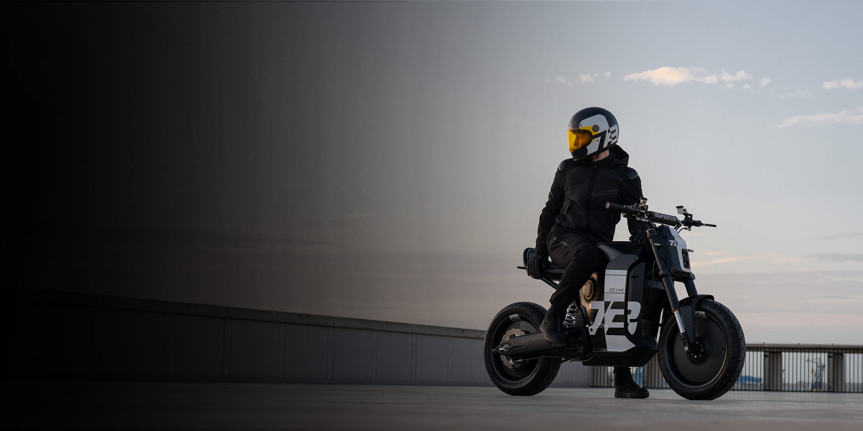 The Super73-C1X in black and white shown with a rider sitting on the bike on a concrete pathway