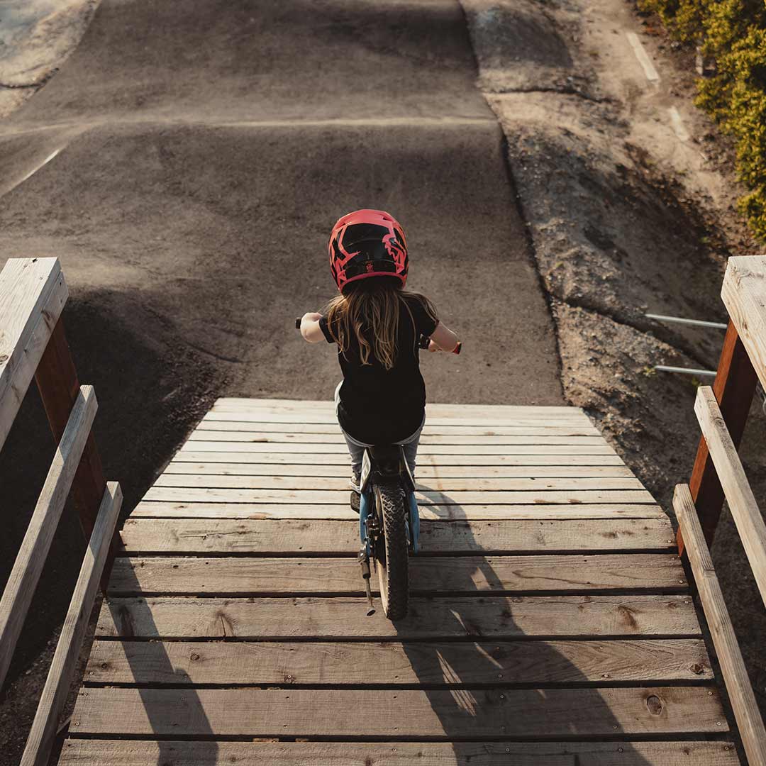 Young rider on her blue SUPER73 K1D kid's e bike about to drop in, sitting looking down at the track