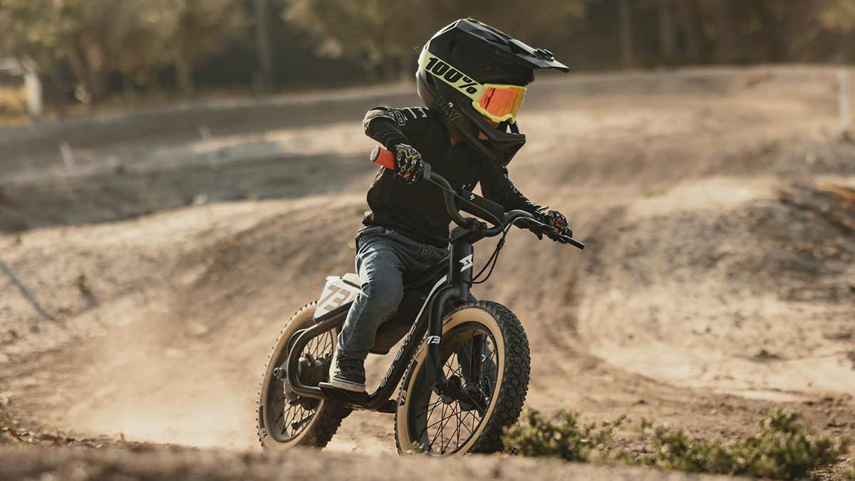 Young rider on his black SUPER73 K1D kid's e bike on a dirt track coming aggressively around a corner