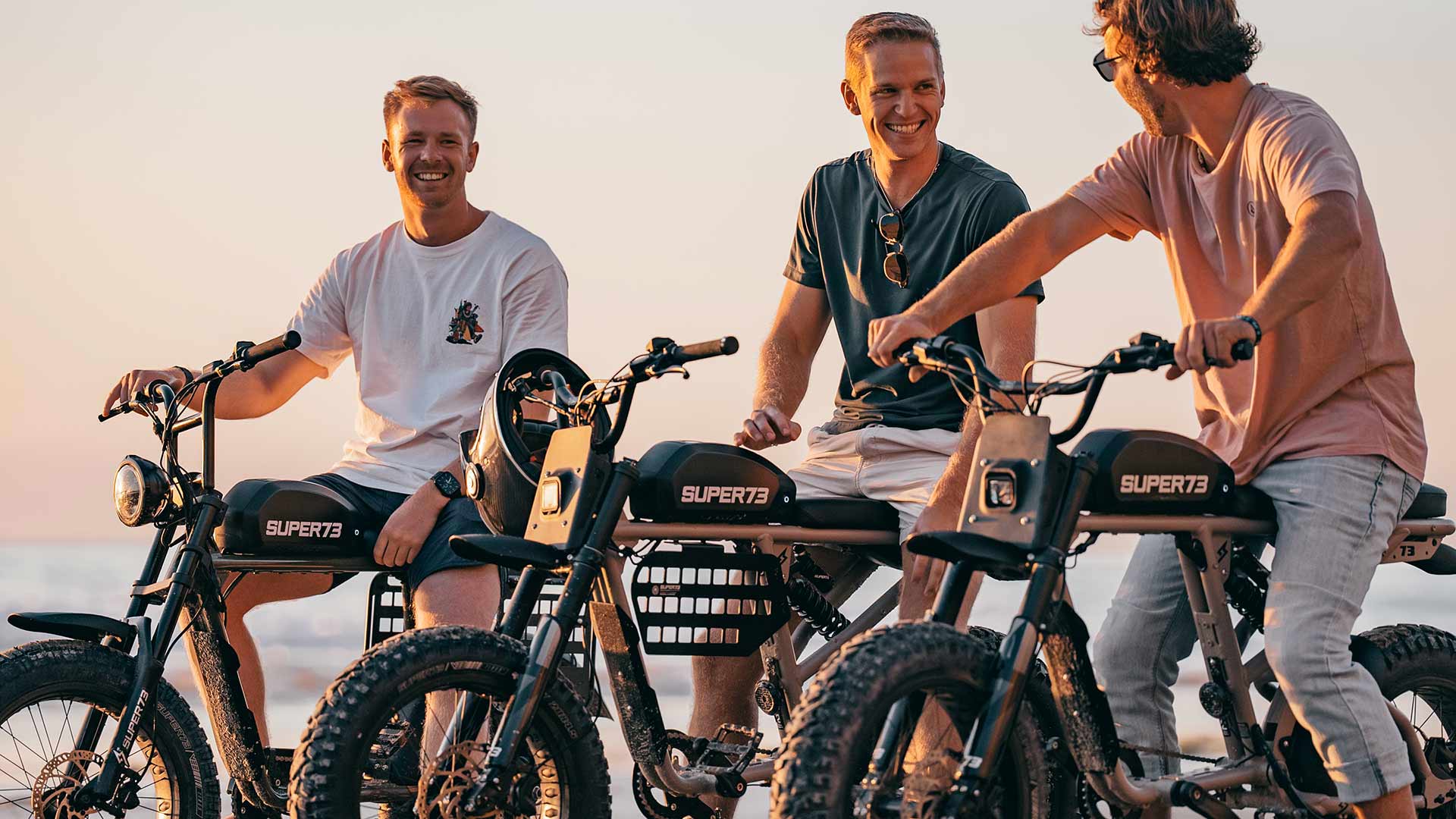 3 guys sitting on their Super73 at the beach watching the sunset. 