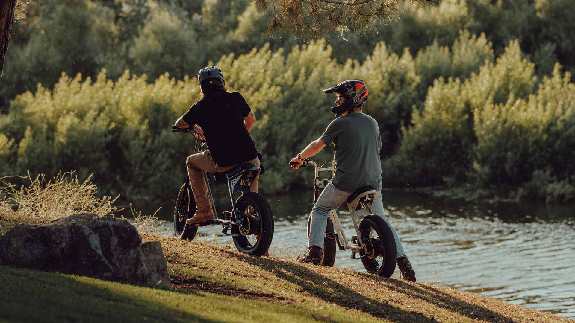 Two young men riding their SUPER73 e-bikes along the riverbank. 