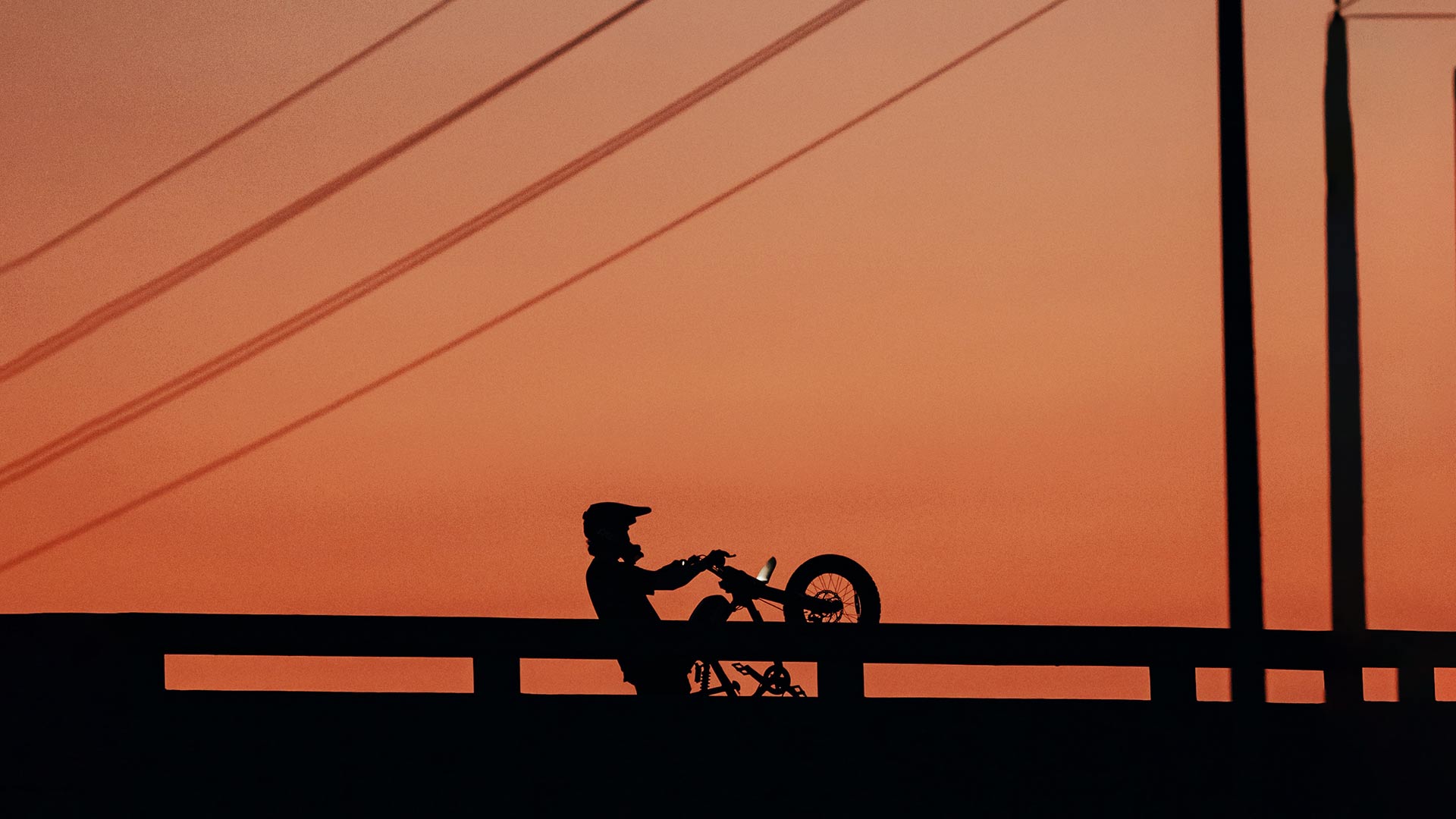 Silhoutte of a rider on a Super73 ebike doing a wheelie in front of an orange sky