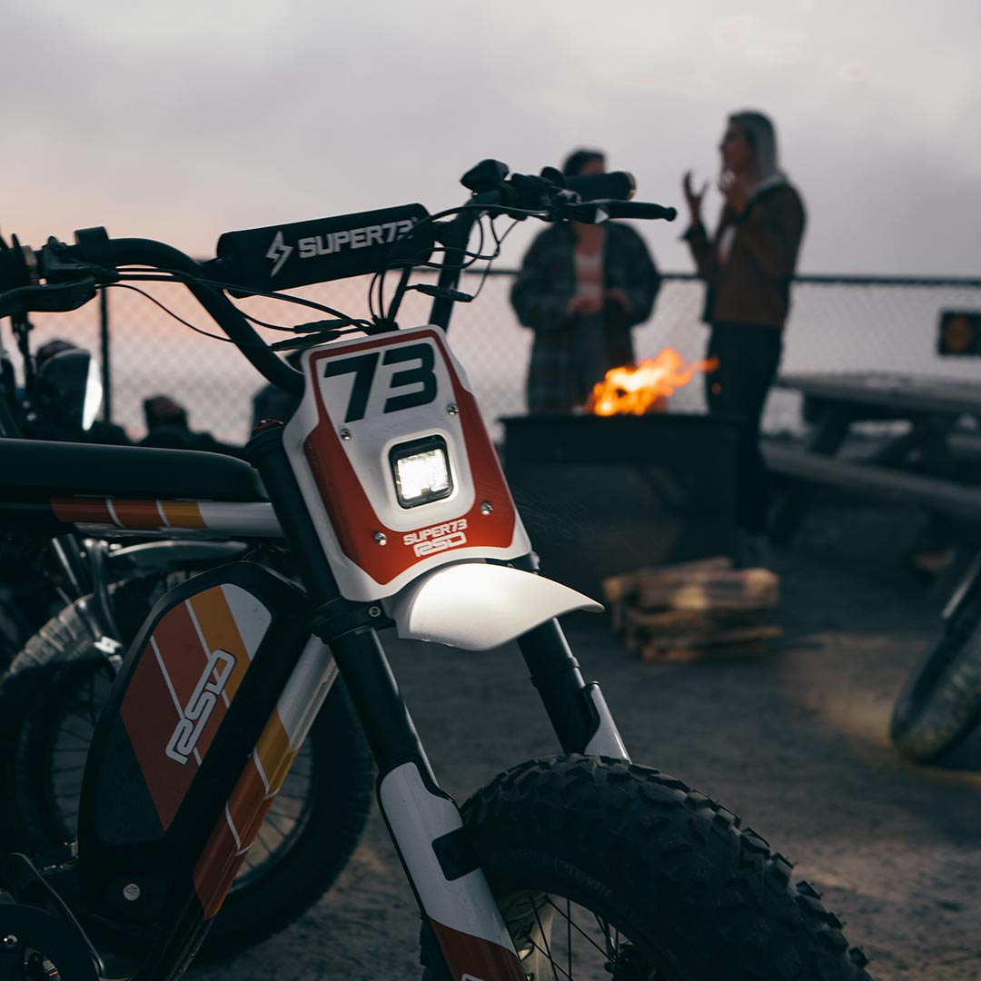 Front side view of the RSD x SUPER73 RX Malibu at night in front of a campfire 