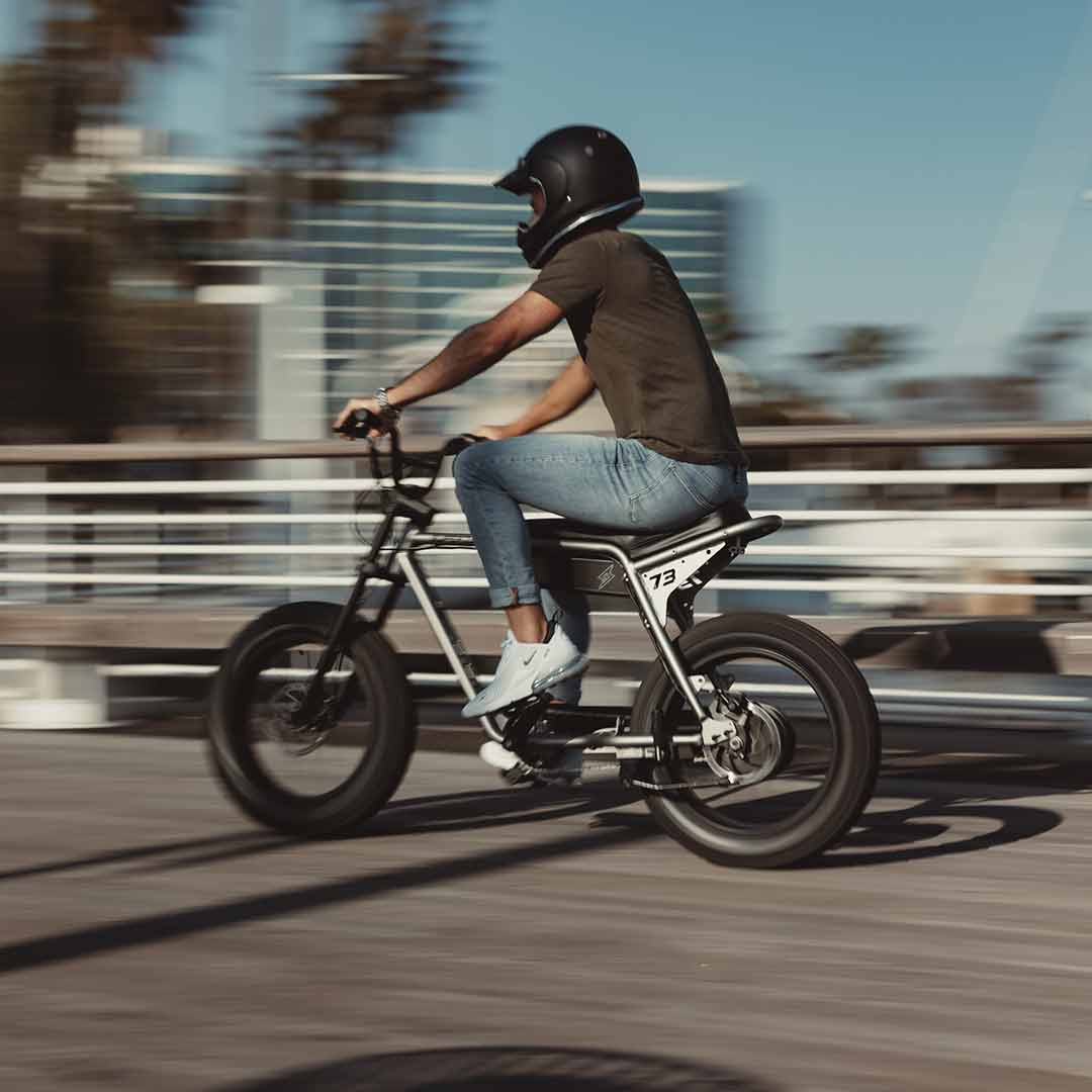 A young man cruising by on his super73 metallic aluminum zx with a helmet on