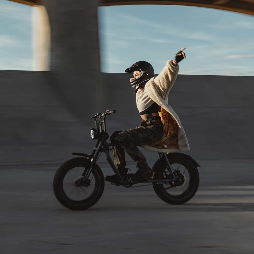 Young woman riding a SUPER73 S2 ebike with her arms in the air next to the Sepulveda Dam