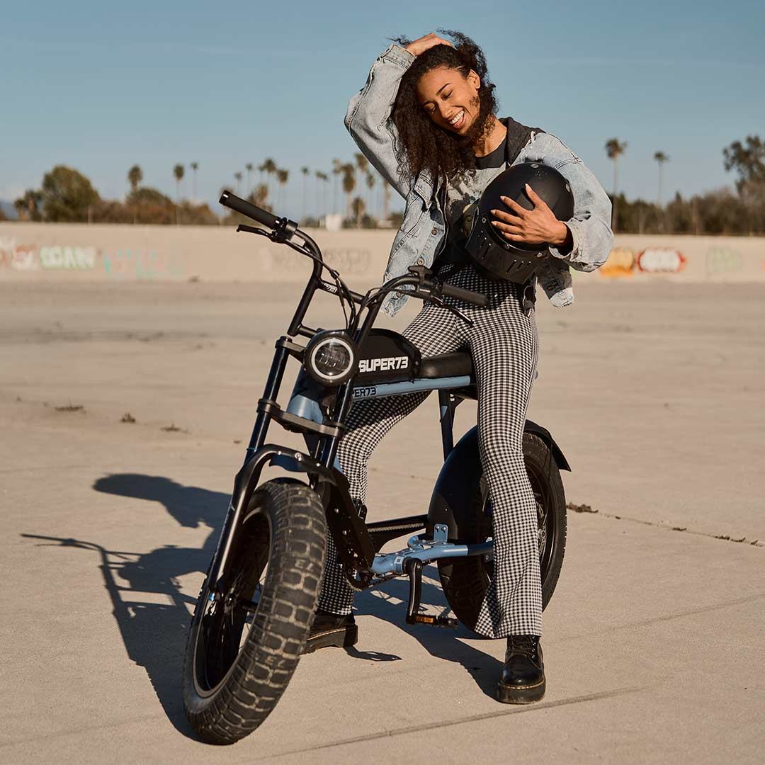 Young woman sitting on a SUPER73 S2 ebike playing with her hair on a sunny day