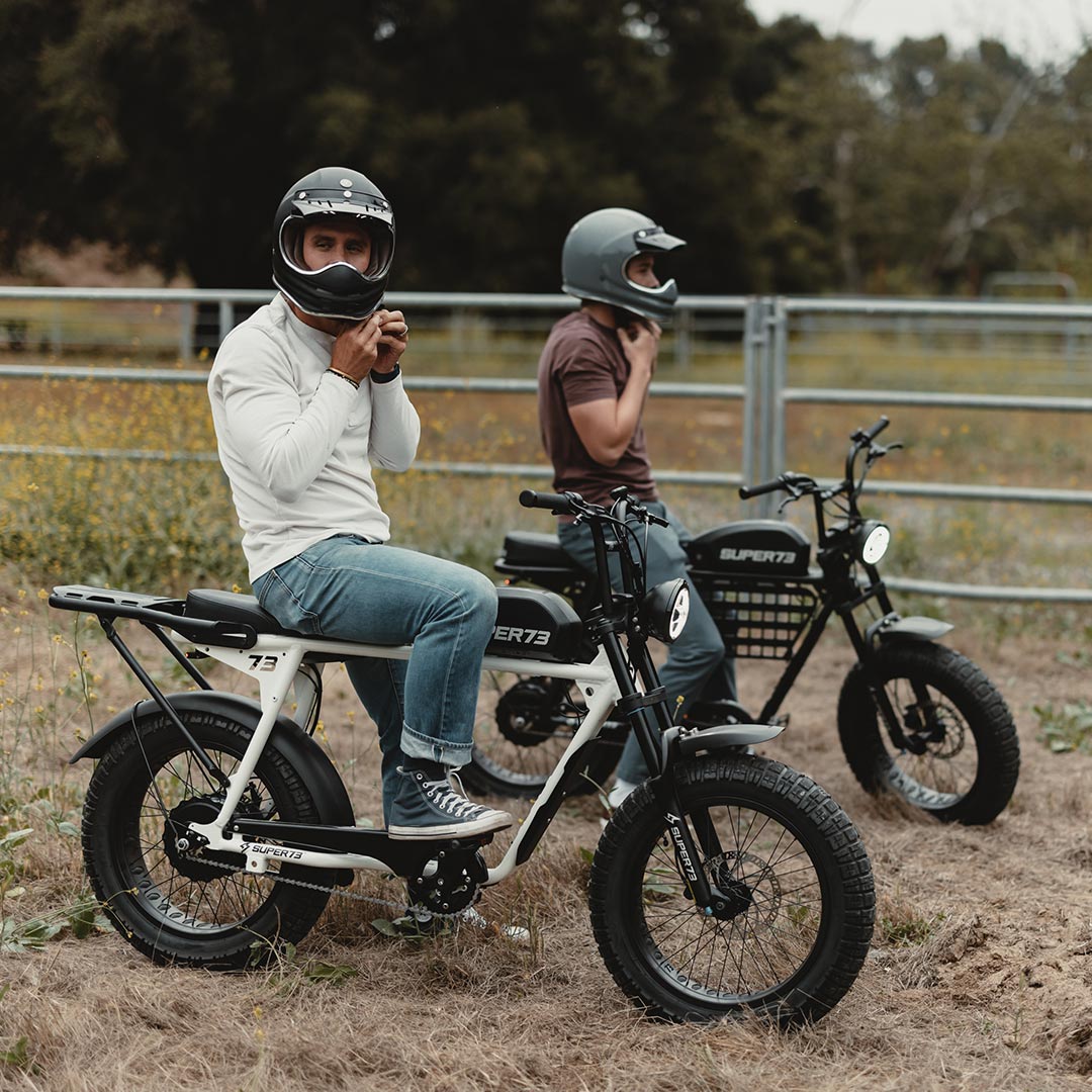 Dad and son sitting on their SUPER73 S2 ebikes in a flower field next to a railing